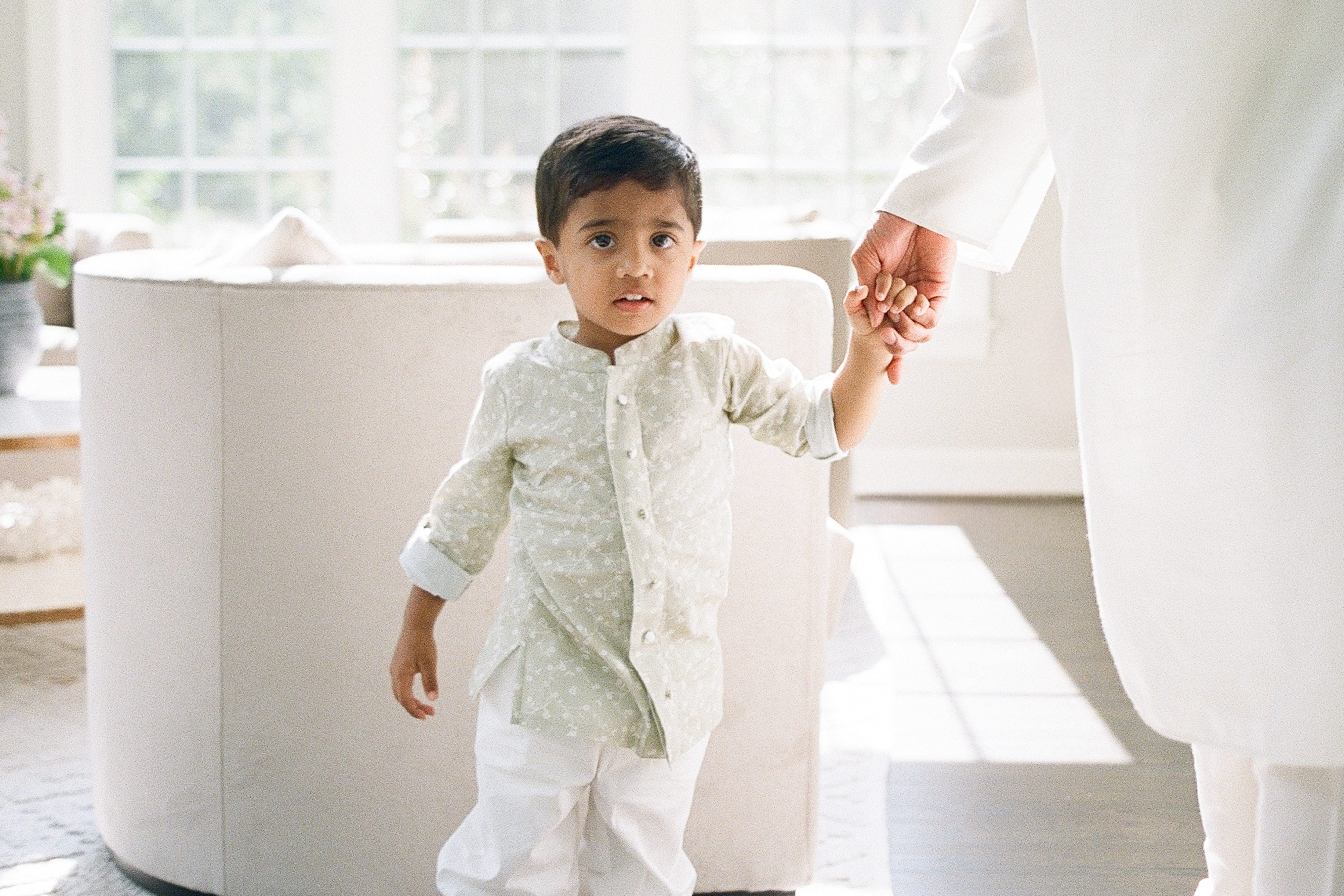 Child holding hands with an adult in a bright, minimalistic room.