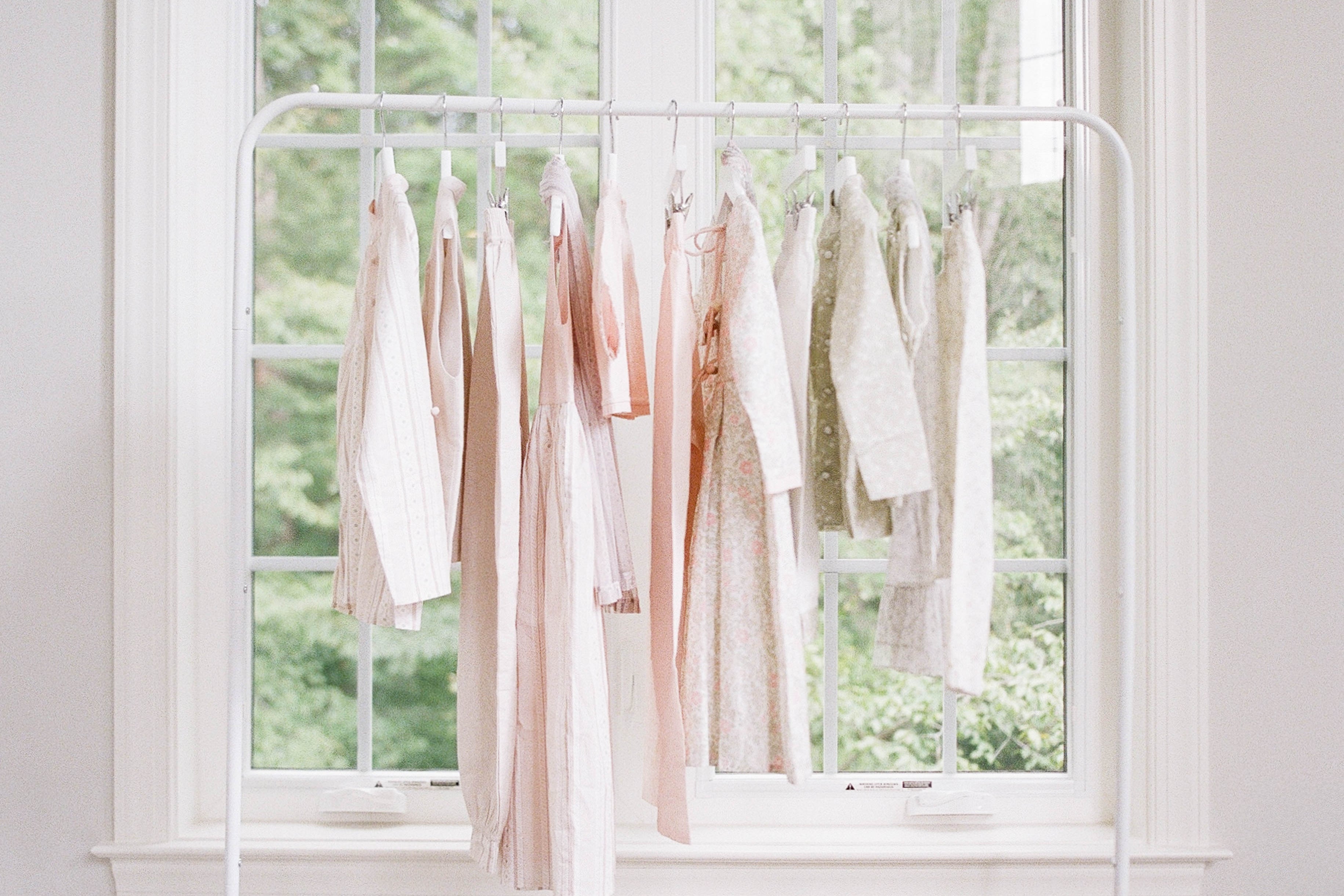 White clothing rack with pink and white garments against a window with greenery outside